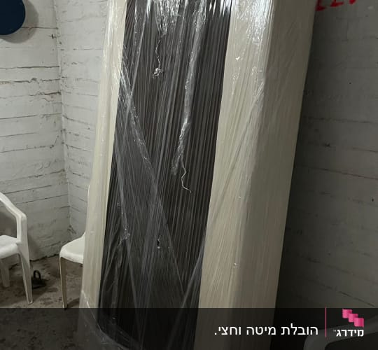 חפץ גדול עטוף בניילון בחדר עם כיסאות פלסטיק לבנים